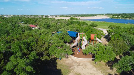 Lakeside Brushy Creek Lake Park with modern tower playground, embankment waterfront retaining wall in lake background, 90-acre park in Cedar Park with nature trails, suburbs Austin, aerial view. USA