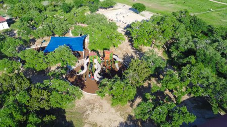 Sand volleyball courts, modern tower playground tall slide with diverse kids playing, lush greenery tree canopy at Brushy Creek Lake Park, 90-acre park in Cedar Park, suburbs Austin, aerial view. USA