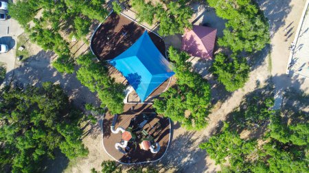 Diverse kids playing at playground with sail shades, soft rubber flooring, tree canopy in Brushy Creek Lake Park, lush greenery community 90-acre park in Cedar Park, suburbs Austin, aerial view. USA
