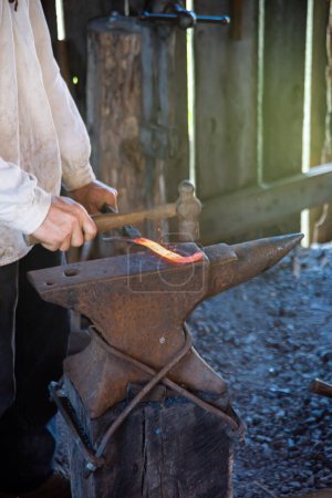 Blacksmith man hand using hammer to forge cast iron melting on medieval anvil traditional trade workshop, Mansfield, Missouri, anvil with smooth working surface of hardened steel strike forging. USA