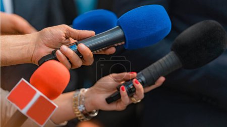 Journalists hold microphones in their hands at a press conference.