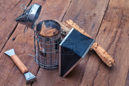 Photo for The set also comes with a smoker, hive tool, and bee brush, all neatly arranged on a wooden table. - Royalty Free Image