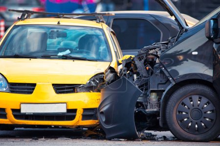 Foto de Esta foto captura las secuelas de un accidente de coche entre un vehículo azul y amarillo. Escombros ensucian la carretera mientras el personal de emergencia atiende la escena - Imagen libre de derechos