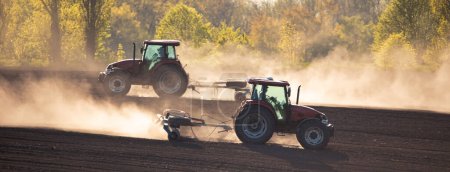 Téléchargez les photos : Avec l'aide d'un tracteur robuste, un cultivateur brise le sol, assurant des conditions optimales pour la croissance des cultures - en image libre de droit