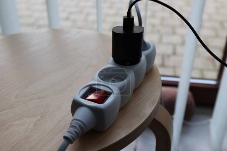 A portrait of a white power strip with a red on off button with a black charger in it. The sockets of the device are turned off and the light in the button is off to indicate it.