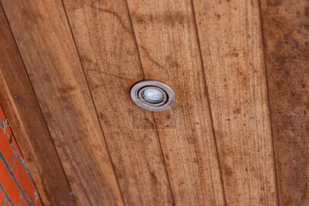 Foto de Un retrato de un punto de luz sellado por el clima colocado en los tablones de madera de un techo sobresaliente. La lámpara está apagada.. - Imagen libre de derechos