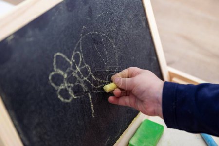 Photo for A close up portrait of a toddler scribbling, drawing or doodling a bit on a chalkboard. The child is writing on the blackboard and has a yellow piece of chalk in its hand. - Royalty Free Image