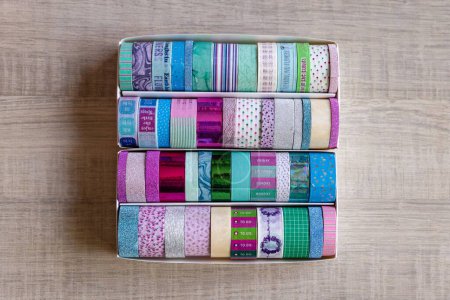 Foto de Una caja llena de rollos coloridos de cinta washi con diferentes colores, patrones y texturas en una mesa de madera. Las cintas están listas para ser utilizadas para decorar un interior, regalo, poste o tarjeta de regalo. - Imagen libre de derechos