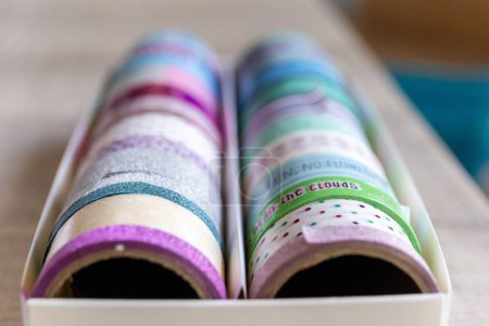 Foto de Una caja llena de rollos coloridos de cinta washi que tienen diferentes texturas, patrones y colores en una mesa de madera. Las cintas están listas para ser utilizadas para decorar un interior, regalo o postal, regalo. - Imagen libre de derechos