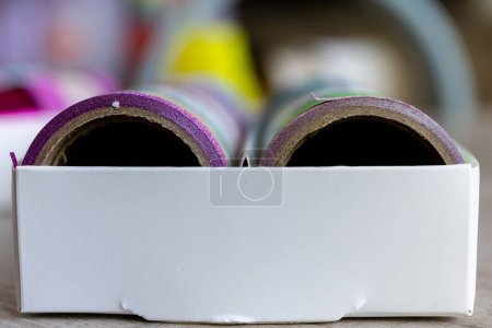 Foto de Una caja llena de rollos coloridos de cinta washi que tienen diferentes texturas, patrones y colores en una mesa de madera. Las cintas están listas para ser utilizadas para decorar un interior, poste o tarjeta de regalo, regalo. - Imagen libre de derechos