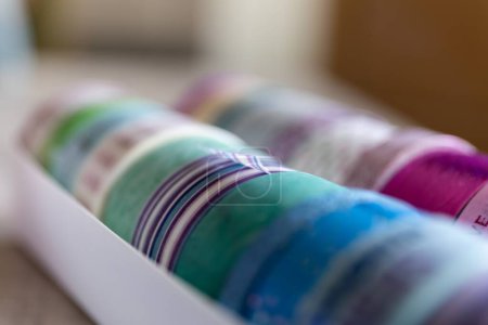 Foto de Un primer plano de cinta washi colorido en diferentes patrones y colores en una caja. Los rollos decorativos están listos para usar para decorar un poste o tarjeta de regalo, regalo o para usar para el diseño de interiores como en una pared.. - Imagen libre de derechos