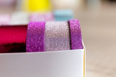 Foto de Un retrato frontal de unos rollos de cinta washi en una caja. Las cintas decorativas son de color rosa y púrpura y tienen brillo en ellas, listas para decorar un regalo, interior, pared, poste o tarjeta de regalo.. - Imagen libre de derechos