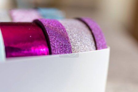 Foto de Un retrato de cerca de unos rollos de cinta washi en una caja. Las cintas decorativas son de color rosa y púrpura y tienen brillo en ellas, listas para decorar un regalo, interior, pared, poste o tarjeta de regalo.. - Imagen libre de derechos