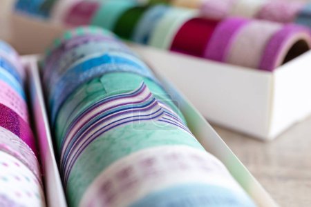 Foto de Un retrato de cinta washi colorida en diferentes patrones y colores en una caja. Las cintas decorativas están listas para usar para decorar un regalo, poste o tarjeta de regalo o para usar para el diseño de interiores como en una pared.. - Imagen libre de derechos