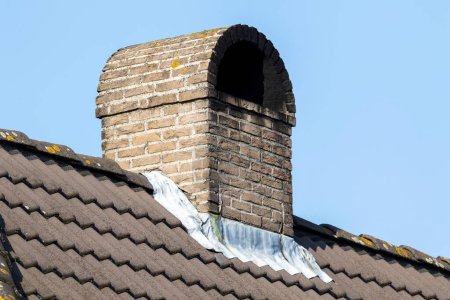 Téléchargez les photos : Portrait d'une cheminée en brique sur un toit carrelé par une journée ensoleillée. la construction est arrondie sur le dessus contre la pluie. l'intérieur de la cheminée est plein de suie noire, de fumée noire ou de crasse. - en image libre de droit
