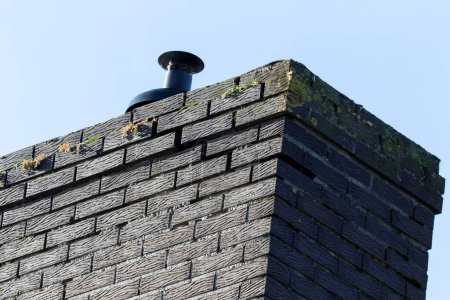 Photo for A closeup portrait of a large black chimney on the roof of a house, which needs to be repaired and needs a restoration, because there is a crack visible in between some of the bricks. - Royalty Free Image