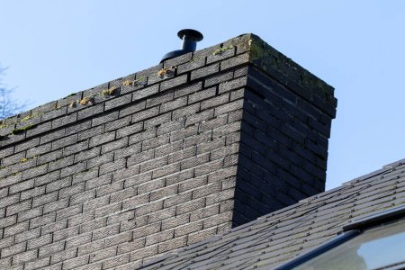 Photo for A portrait of a large black chimney on the roof of a house, which needs to be repaired and needs a restoration, because there is a crack visible in between some of the bricks. - Royalty Free Image