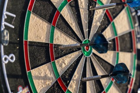 A close up portrait of a dartboard game outside on a sunny day, with darts sticking in it. the bull is also visible. the darts are ready to be thrown in a game or match.
