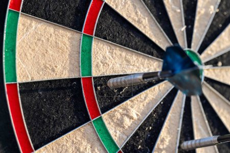 A portrait of a part of a dartboard game outside on a sunny day, with darts sticking in it. the bull is also visible. the darts are ready to be thrown in a game or match.