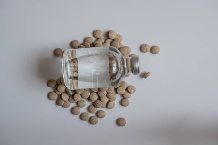 Foto de Un frasco grande de inyección y una pastilla, colocados juntos, sobre un fondo blanco. - Imagen libre de derechos