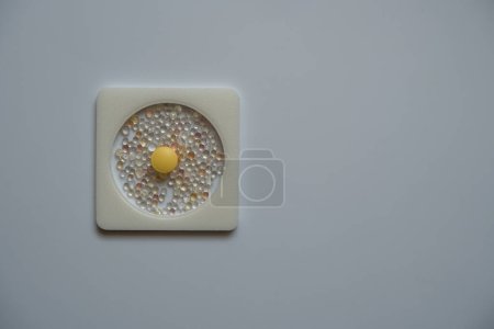 Foto de Una pastilla amarilla, colocada en un marco cuadrado, y una tableta desecante. - Imagen libre de derechos