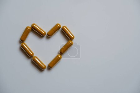 Foto de Varias cápsulas marrones, dispuestas en forma de corazón, sobre un fondo blanco. - Imagen libre de derechos