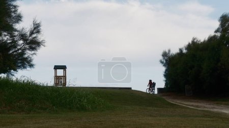 Photo for Woman on bicycle with child on seaside background and lifeguard tower - Royalty Free Image
