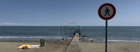 Foto de Muelle en una playa con toalla y silla de plástico con señal de tráfico resaltada - Imagen libre de derechos