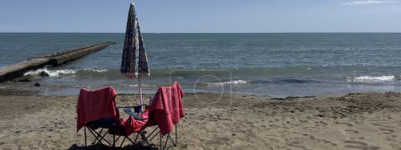 Photo for Pier on a beach with closed umbrella and towel on a chair and sea background - Royalty Free Image