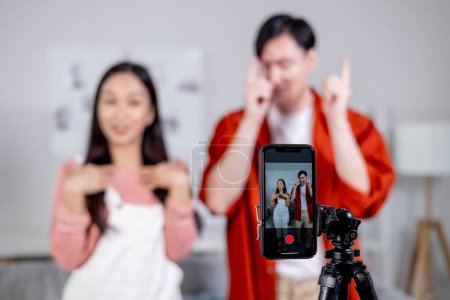 Asian young couple tiktoker creating their dancing video with smartphone camera and tripod. Cute man and woman making a vertical video content to share on social media