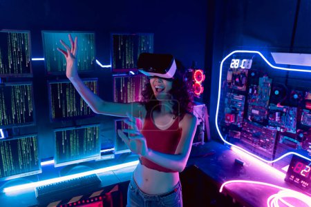 Téléchargez les photos : Young Asian woman using virtual reality glasses in the dark room with neon lighting full of computers and technology stuff - en image libre de droit