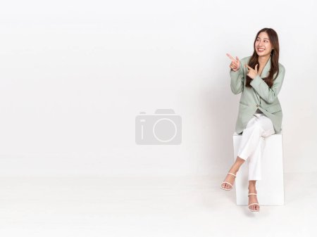 Foto de Feliz alegre joven mujer de negocios asiática en traje y pantalones sentados en la caja blanca aislado sobre fondo blanco - utilizado para la publicidad y la promoción de marketing - Imagen libre de derechos