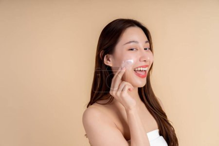 Photo for Closeup portrait of a face of the young Asian girl with a healthy facial skin rubbing her face with facial white cream in studio background. Skin care and dermatology concept. - Royalty Free Image