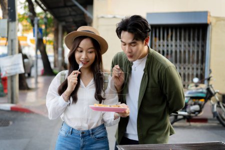 Photo for Asian couple traveler wearing a casual wear and hat in relationship buying a dessert snack on street food market in the evening. Backpacker traveling in Bangkok, Thailand. - Royalty Free Image
