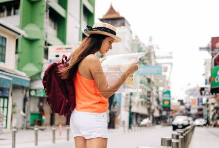 Foto de Serio joven hispana morena mujer sosteniendo mapa en la calle de vacaciones con mochila. - Imagen libre de derechos
