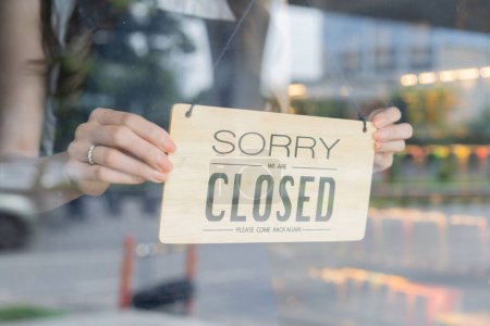 Ladeninhaberin dreht Schild des Start-up-Cafés und Restaurants durch das Türglas und schließt den täglichen Service