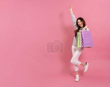 Téléchargez les photos : Portrait d'une jeune femme asiatique heureuse shopper souriant tenant des sacs à provisions en fond rose - Concept de femme shopping en ligne - en image libre de droit