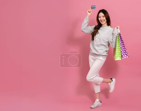 Photo for Portrait of a happy Asian young female shopper smiling holding a credit card while having shopping bags on other hand in pink background - Online shopping with online payment concept - Royalty Free Image