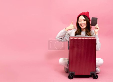 Téléchargez les photos : Jeune voyageuse asiatique avec un sourire donne pouces levés. Profiter d'un voyage de vacances heureux, tenant son passeport en fond rose isolé. Représenter la joie du voyage et de l'aventure - en image libre de droit