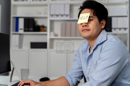 Téléchargez les photos : Jeune homme d'affaires asiatique adulte ayant AIDE note collante sur son visage dans le contexte de bureau. Homme d'affaires est ennuyé, frustré, malheureux, et bourreau de travail. - en image libre de droit