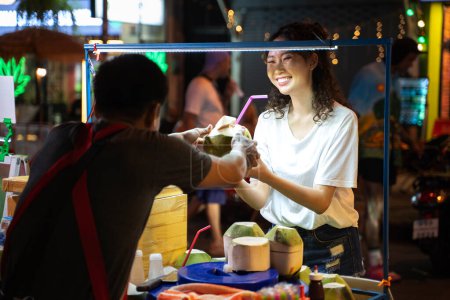Photo for Portrait of happy relaxing Asian solo hipster traveller receiving a coconut drink with a happy smile on street in Bangkok, Thailand. Female tourist exploring Southeast Asia. - Royalty Free Image