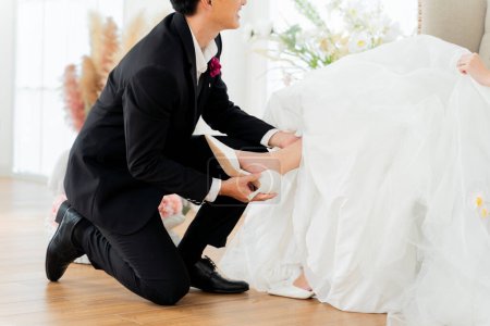 Téléchargez les photos : Un marié dévoué aide sa mariée avec des chaussures, un geste doux d'amour et de soutien - en image libre de droit