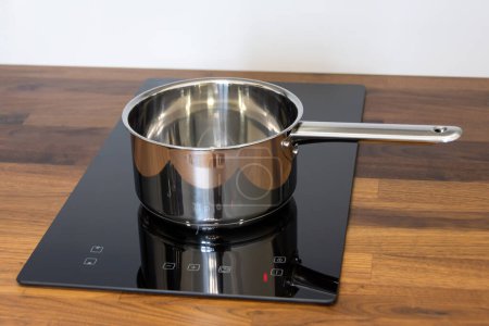 Téléchargez les photos : Casserole louche sur une plaque à induction intégrée dans un plan de travail de cuisine en bois - en image libre de droit