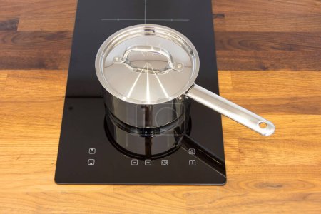Photo for Saucepan ladle with lid on an induction hob built into a wooden kitchen worktop, top view - Royalty Free Image