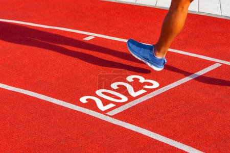 Der Läufer überquert die Ziellinie auf einem roten Laufband mit der Nummer 2023. Neujahrskonzept, Schritt