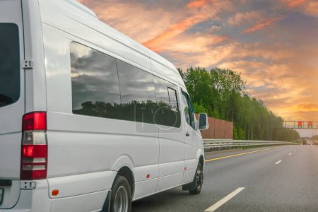 Photo for White modern passenger charter van with a small delivery moves fast on the highway to the urban suburbs. Business distribution and logistics express service. Mini bus rides along the highway - Royalty Free Image