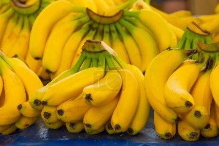 Plátanos amarillos maduros se encuentran en un puesto de mercado con otras frutas en el fondo
