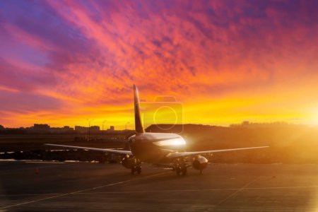 Téléchargez les photos : Le fuselage brillant de l'avion et sa silhouette dans le parking de l'aéroport le soir au beau coucher de soleil avec des nuages texturaux - en image libre de droit