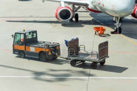 Photo for Special car and empty baggage cart next to the plane - Royalty Free Image