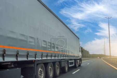 Téléchargez les photos : Camion long rideau inclinable remorque latérale de transport sur la route jour ciel bleu - en image libre de droit